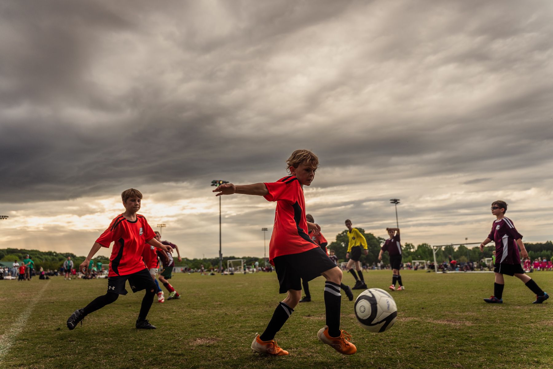 Young soccer players mid-game under a dramatic cloudy skying