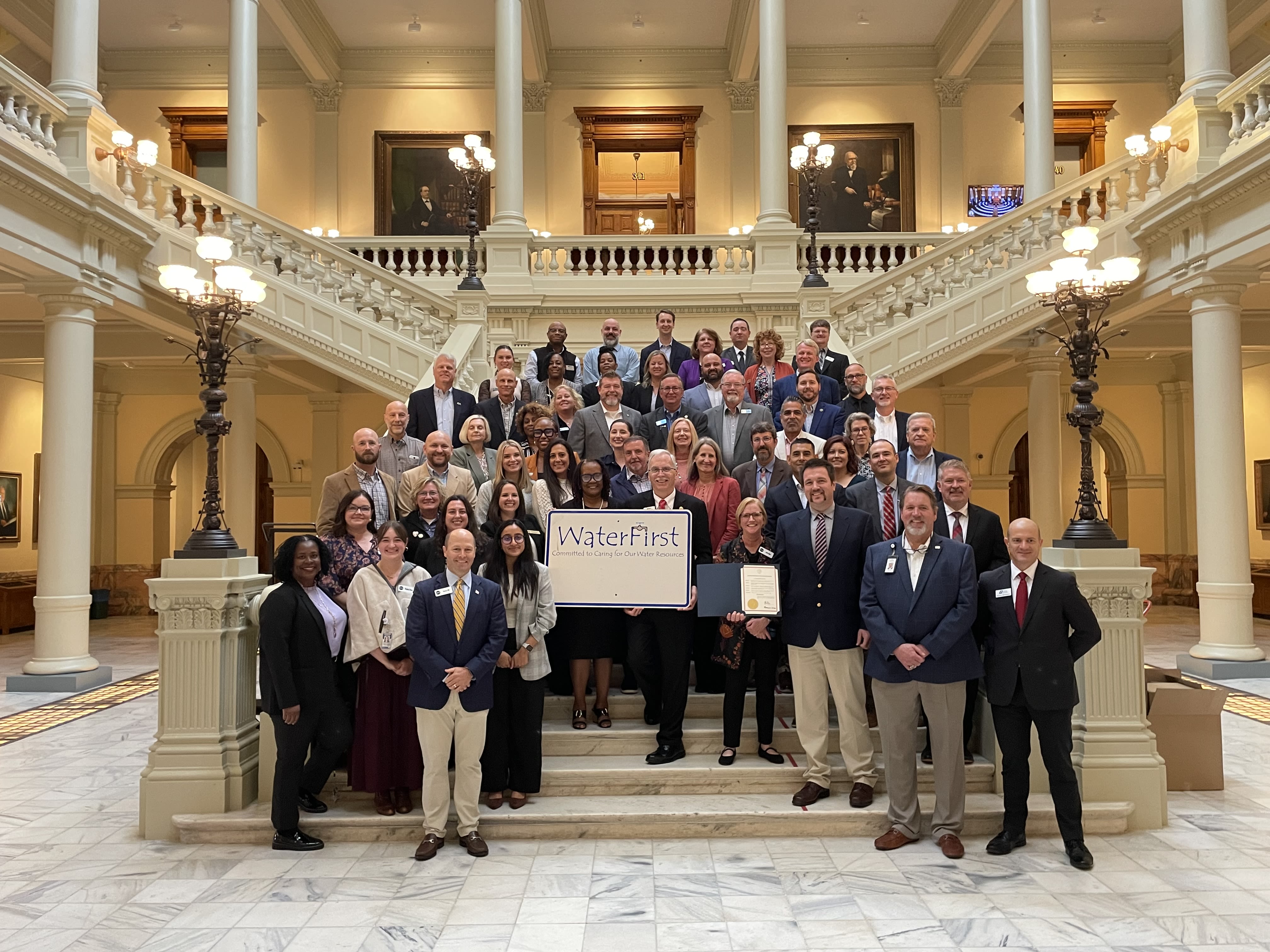 Water First designees pose together on the steps of the State Capitol rotunda with a Water First sign