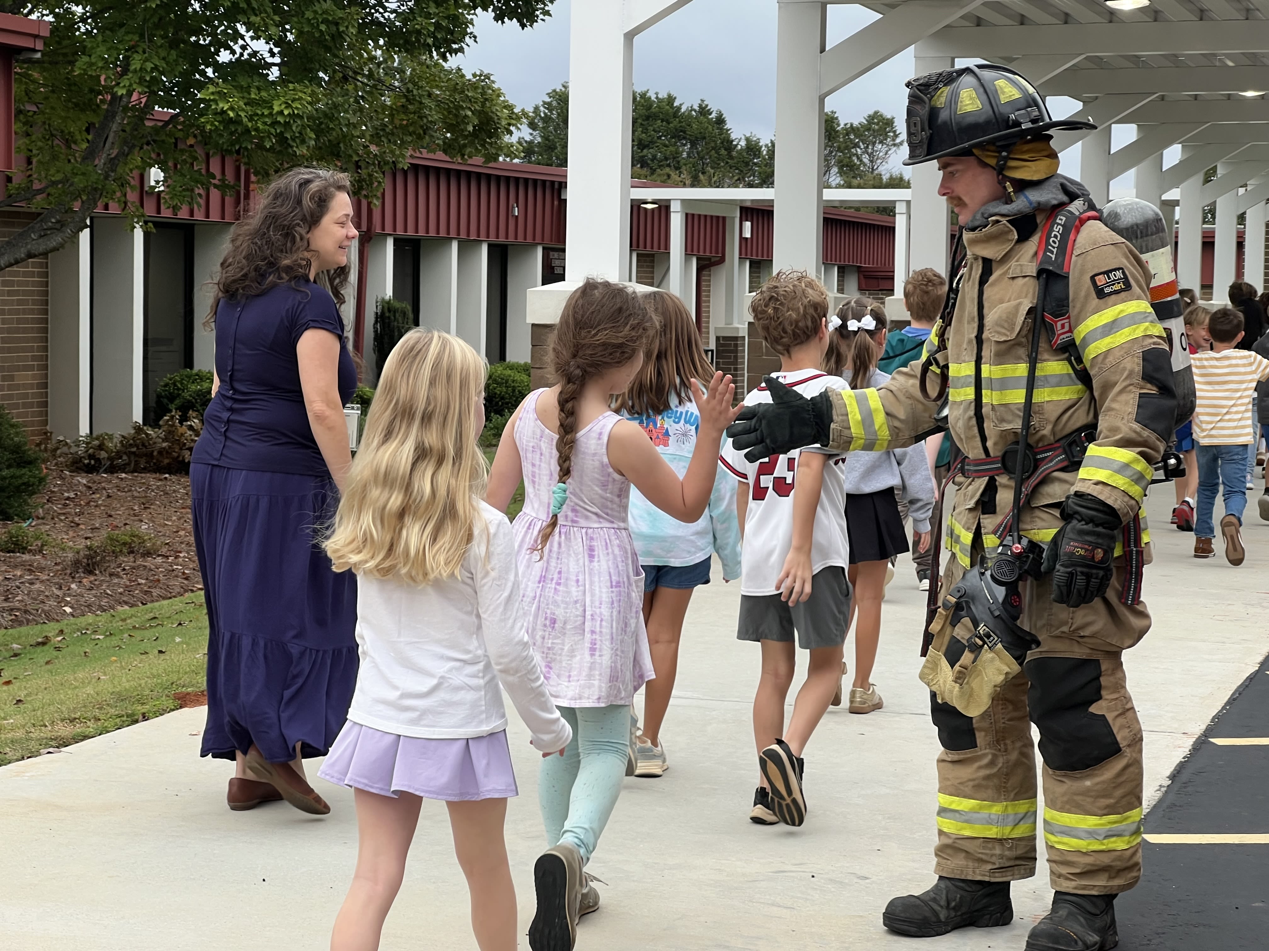 Firefighter high fives elementary students walking into school